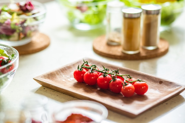 Mise au point sélective de la plaque en bois avec des tomates cerises. Épices et bols de salades