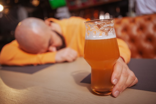 Mise au point sélective sur un verre à bière dans la main d'un homme ivre au pub. Alcoolique, dépendance, concept de consommation d'alcool