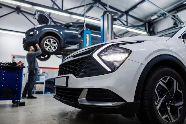 Mise au point sélective sur une voiture au premier plan avec un mécanicien automobile réparant une autre voiture en arrière-plan flou