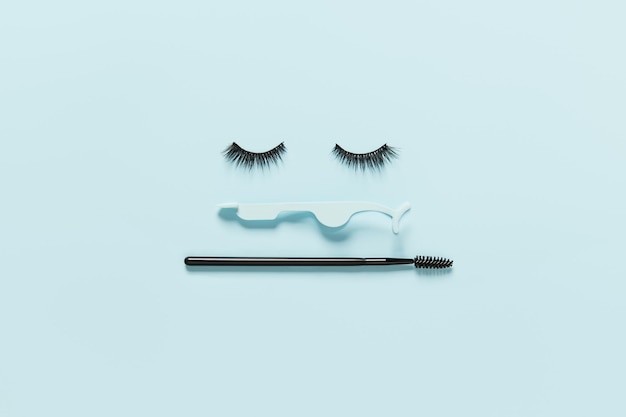 Mise en page créative avec applicateur de cils et brosse à mascara yeux fermés sur fond bleu pastel