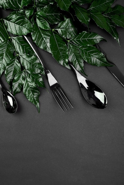 Mise en page créative faite de feuilles vertes et de couverts noirs cuillère fourchette couteau avec espace de copie Mise à plat Nature concept de restaurant de printemps ou d'été