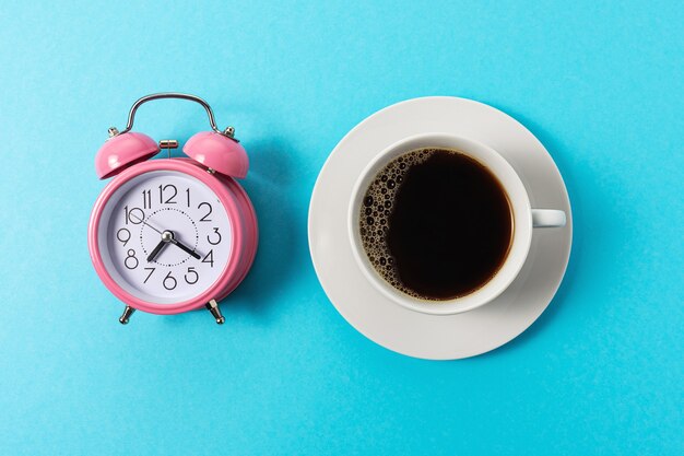 Mise en page créative faite avec une tasse de café et un réveil sur fond bleu.