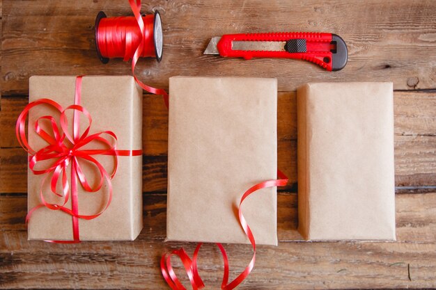 La mise en page à plat de boîtes d'artisanat, ruban rouge et couteau rouge sur table en bois. Processus d'emballage de cadeaux.