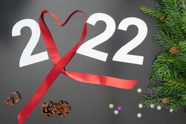 Mise en page sur le thème du Nouveau 2022 avec un ruban rouge, des jouets et des branches d'un sapin de Noël sur fond sombre.