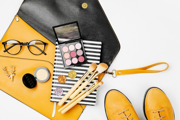 Photo mise à plat d'accessoires de mode féminine, chaussures, produits de maquillage et sac à main sur des couleurs orange. concept de beauté et de mode