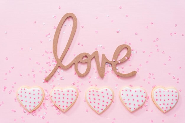 Mise à plat. Biscuits au sucre en forme de coeur décorés de glace royale pour la Saint-Valentin sur fond rose.