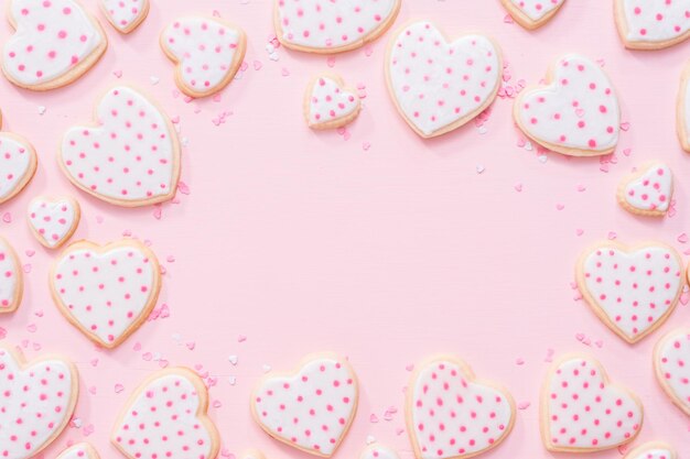 Mise à plat. Biscuits au sucre en forme de coeur décorés de glace royale pour la Saint-Valentin sur fond rose.