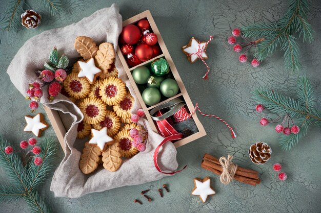 Mise à plat avec des biscuits de Noël et des décorations saisonnières dans une boîte en bois sur une surface rustique grise