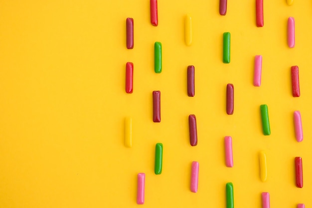 Mise à plat avec des bonbons gommeux colorés avec du sucre sur fond jaune