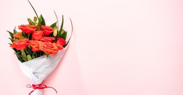 Photo mise à plat. bouquet de roses rouges et de feuilles vertes sur fond rose.