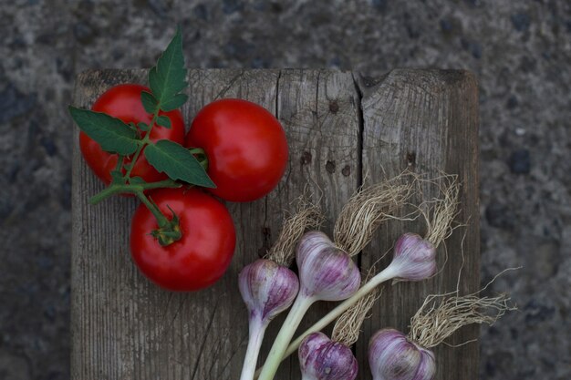 Mise à plat avec branche de tomates rouges et bouquet de bulbes d'ail sur la vieille table en bois