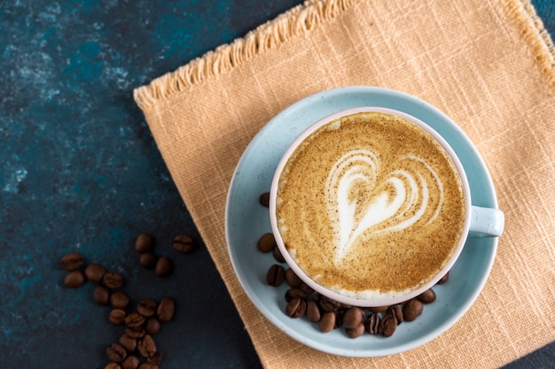 Mise à plat café latte art Cappuccino dans une petite tasse, sur une serviette jaune sur la surface bleue