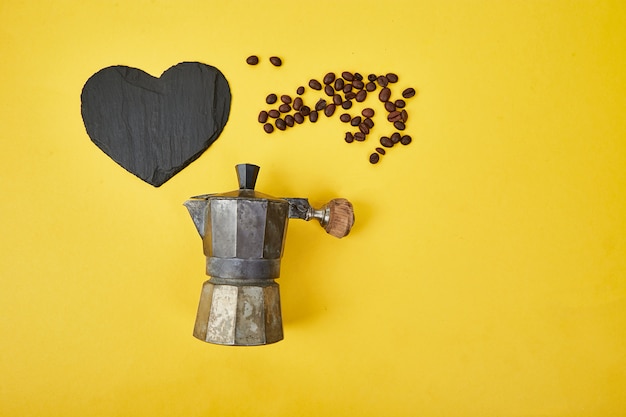 Mise à plat de cafetière et grains de café sur fond jaune.