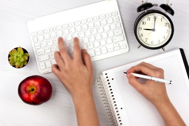 Mise à plat avec clavier blanc, pomme, réveil et mains