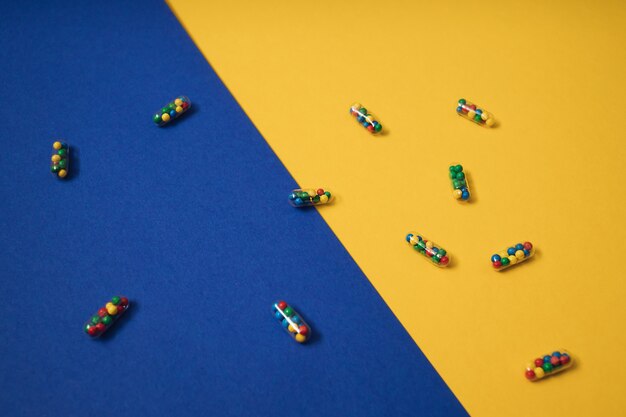 Mise à plat colorée et vibrante de capsules de pilules médicinales remplies de sucre candi saupoudre sur fond jaune et bleu. Concept créatif d'utilisation de médicaments surdosés et de dépendance aux compléments alimentaires.