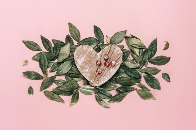 Mise à plat créative de coeur en bois sur rose avec des feuilles naturelles.