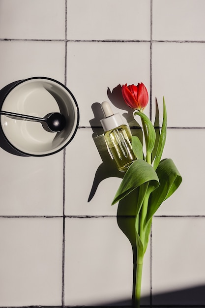 Mise à plat créative de produit cosmétique naturel respectueux de l'environnement dans une bouteille en verre, tulipe rouge, accessoires