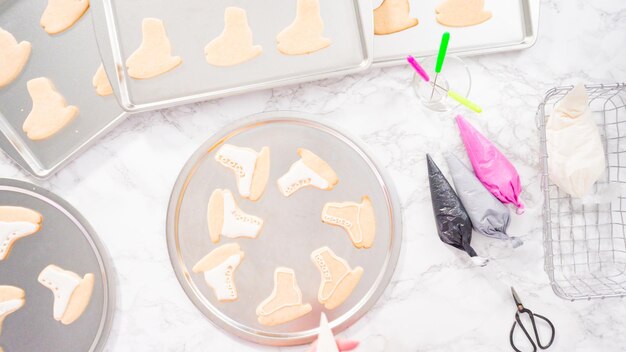 Photo mise à plat. décorer des biscuits au sucre en forme de patin à glace avec du glaçage royal de couleur blanche.