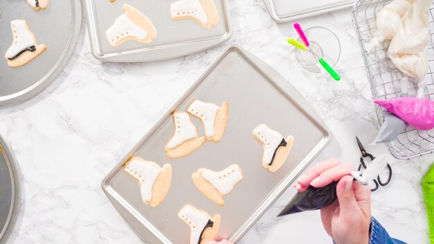 Mise à plat. Décorer des biscuits au sucre en forme de patin à glace avec du glaçage royal de couleur noire.