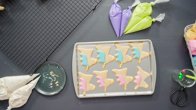 Mise à plat. Décorer des biscuits au sucre de licorne avec du glaçage royal multicolore.