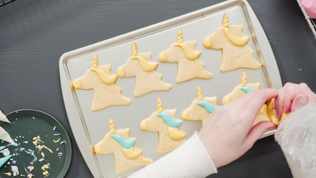 Mise à plat. Décorer des biscuits au sucre de licorne avec du glaçage royal multicolore.