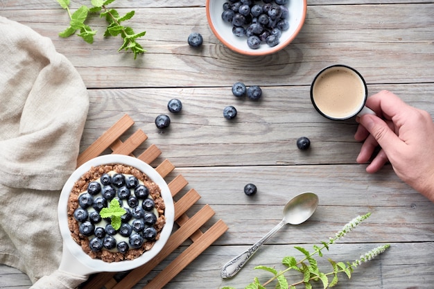 Mise à plat de délicieuses tartelettes aux bleuets avec crème à la vanille et main avec café