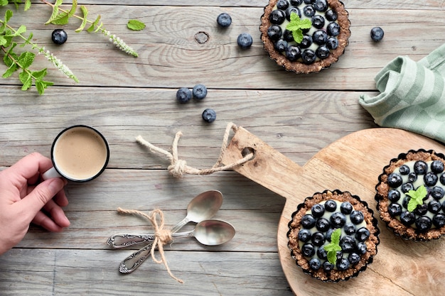 Mise à plat de délicieuses tartelettes aux bleuets avec crème à la vanille et main avec café