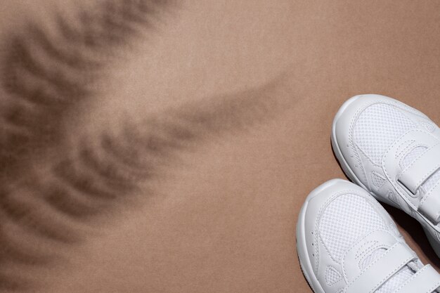 Mise à plat de deux baskets blanches pour adolescents dans le coin avec les ombres d'une fougère ou d'un palmier isolés sur un b ...