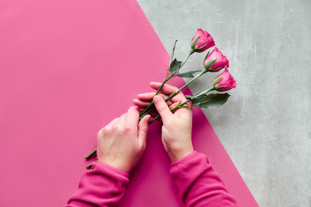 Mise à plat avec deux mains féminines tenant des roses roses sur du papier géométrique diagonal