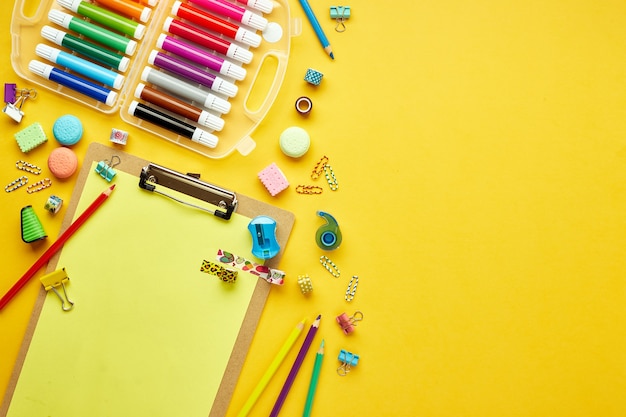 Mise à plat avec diverses fournitures scolaires colorées sur jaune