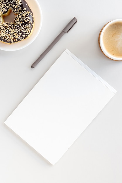 Mise à plat du bureau de l'espace de travail, cahier ouvert, stylo, beignet au café et au chocolat