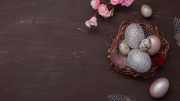 Mise à plat du nid de Pâques et des œufs sur bakcground brun avec des fleurs de fleurs roses copy space