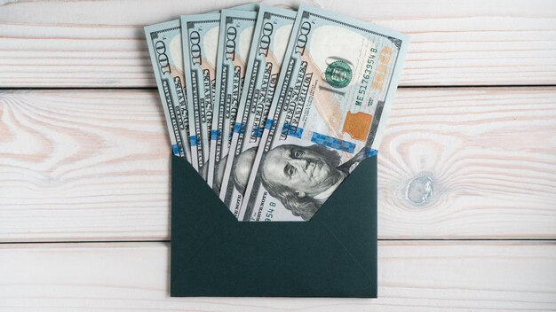 Mise à plat d'une enveloppe verte avec une facture de billets de cent dollars à l'intérieur sur une table en bois gris