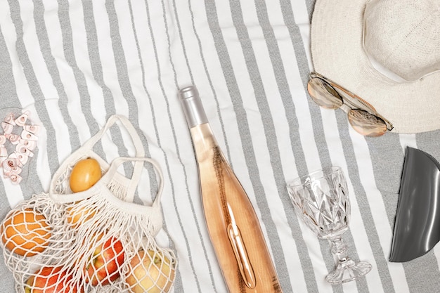 Mise à plat d'été avec des fruits en verre de vin de vin rose dans un sac chapeau de soleil lunettes de soleil sur une serviette de plage