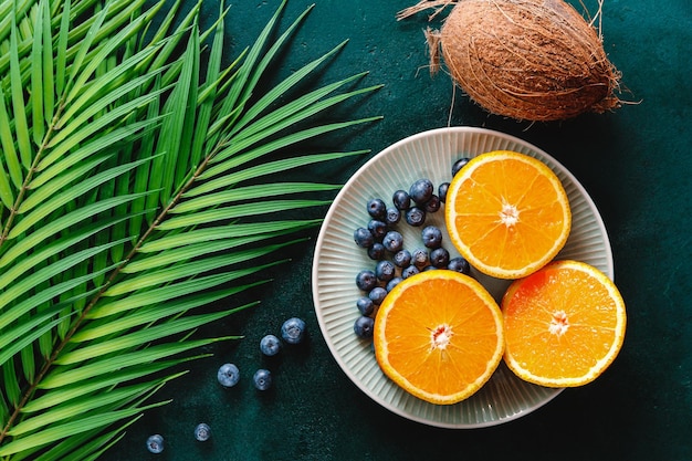 Mise à plat d'été avec des oranges de feuilles de palmier et de la noix de coco sur fond vert foncé