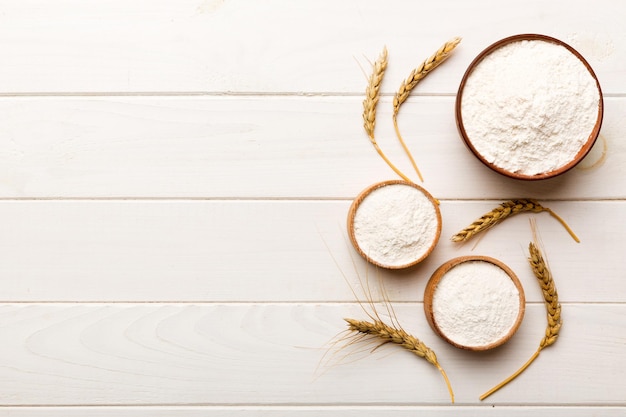 Mise à plat de farine de blé dans un bol en bois avec des épillets de blé sur fond coloré crise mondiale du blé