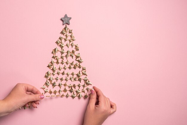 Mise à plat des mains faisant l'arbre de Noël doré avec étoile sur papier rose