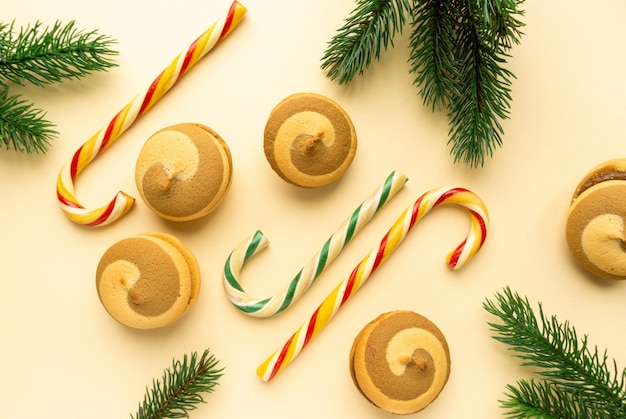 Mise à plat de Noël. Biscuits, canne à sucettes et branches de sapin sur fond beige, vue de dessus.