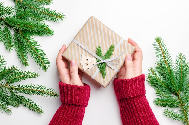 Mise à plat de Noël avec des mains féminines tenant une boîte-cadeau de Noël décorée sur blanc