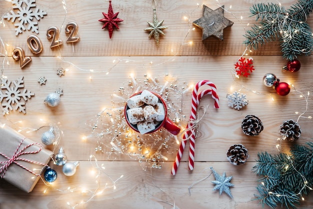 Mise à plat de Noël avec une tasse de chocolat chaud à la guimauve, des cannes de bonbon, des lumières de Noël et des numéros 2022 dorés