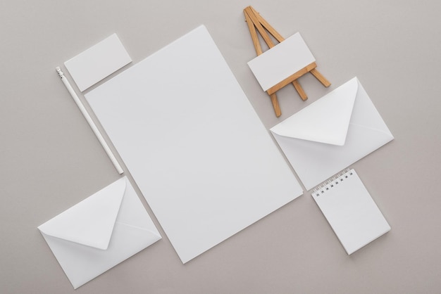 Mise à plat avec des papiers blancs vides et des lettres avec chevalet jouet sur le lieu de travail sur fond gris