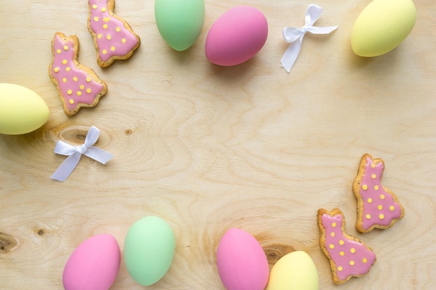 Mise à plat de Pâques. Biscuits faits maison en forme de lapins avec des oeufs colorés sur fond de bois, espace pour le texte