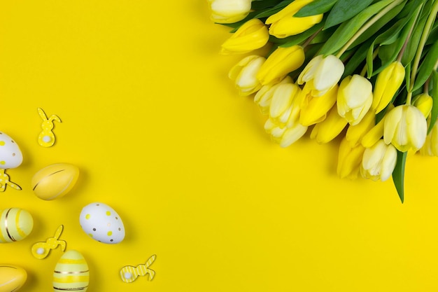 Mise à plat de Pâques avec tulipes jaunes oeufs de Pâques colorés et décoration de lapins sur fond jaune vue de dessus espace de copie