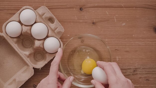 Mise à plat. Pas à pas. Casser des œufs blancs biologiques dans un bol en verre.