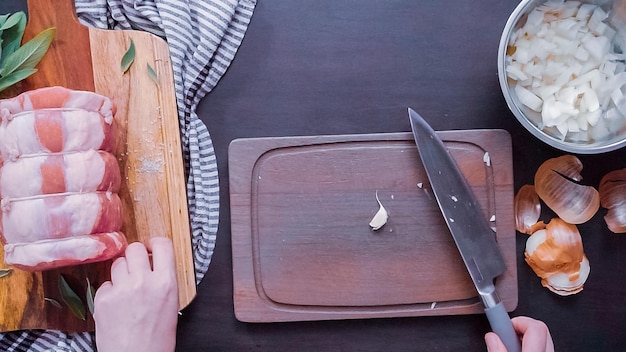 Mise à plat. Pas à pas. Couper l'ail biologique en dés sur une planche à découper en bois.