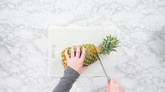 Mise à plat. Pas à pas. Couper l'ananas sur une planche à découper blanche.