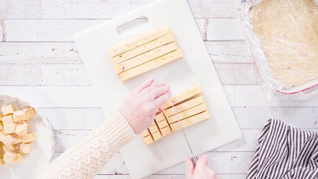 Mise à plat. Pas à pas. Couper le fudge de canne en bonbon fait maison sur une planche à découper blanche.