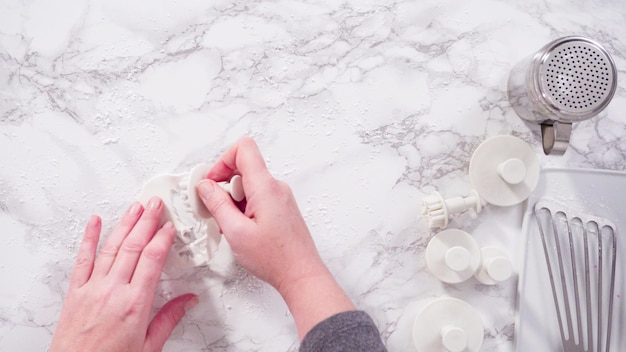 Mise à plat. Pas à pas. Découper des flocons de neige avec des emporte-pièces en fondant blanc sur un comptoir en marbre.