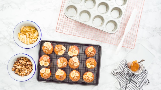 Mise à plat. Pas à pas. Garnir les muffins au pain aux bananes avec du caramel maison, des chips de banane et des noix.