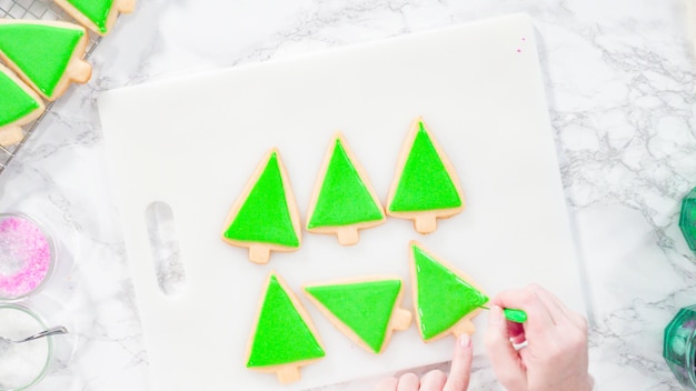 Mise à plat. Pas à pas. Glaçage biscuits au sucre en forme de sapin de Noël avec glaçage royal vert.
